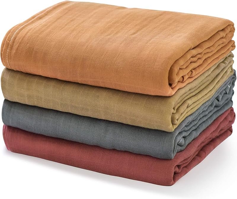 Stack of four folded muslin swaddle blankets in earthy terracotta, olive, sage and dusty rose