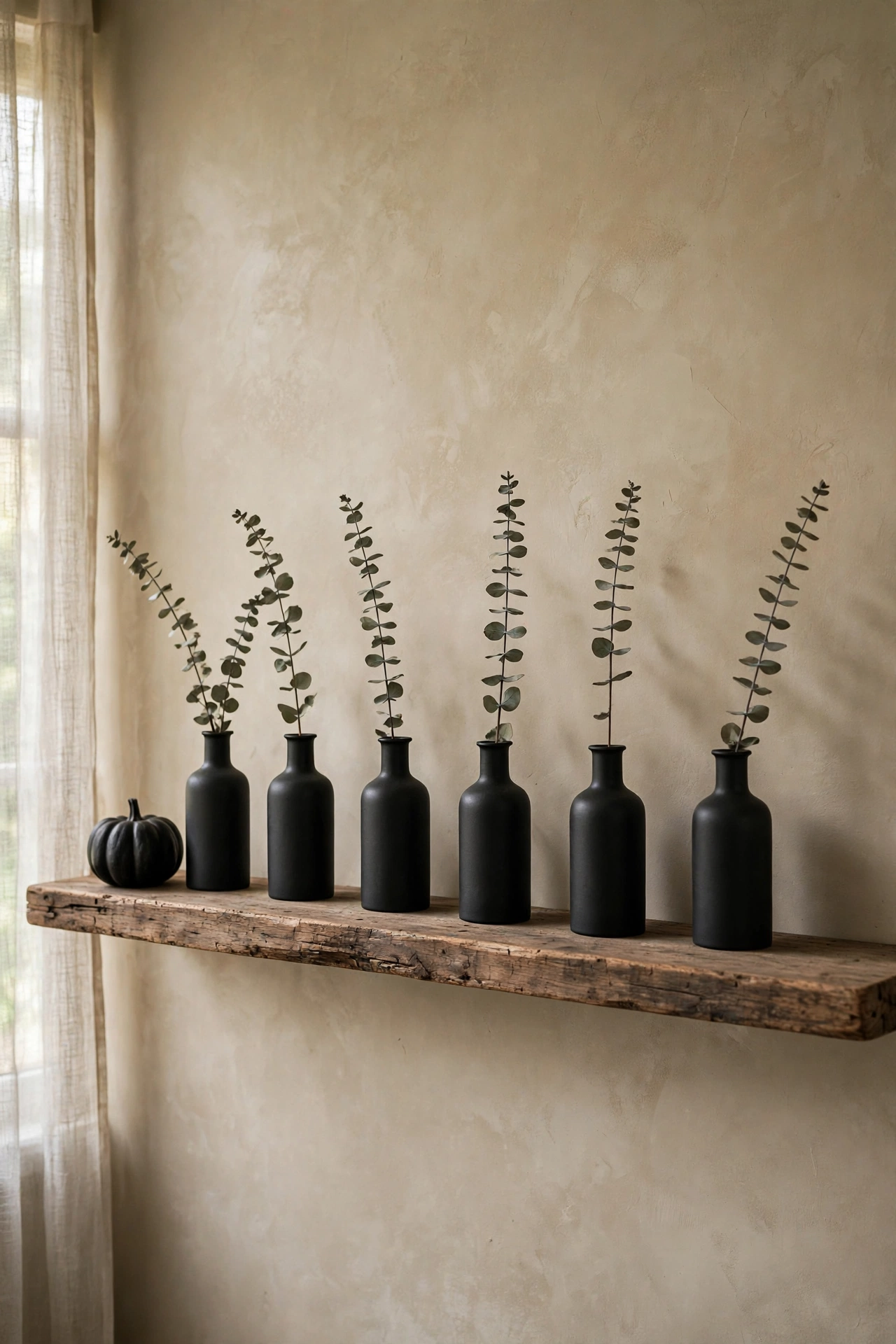 Matte black bud vases with dried eucalyptus sprigs lined along a floating shelf.