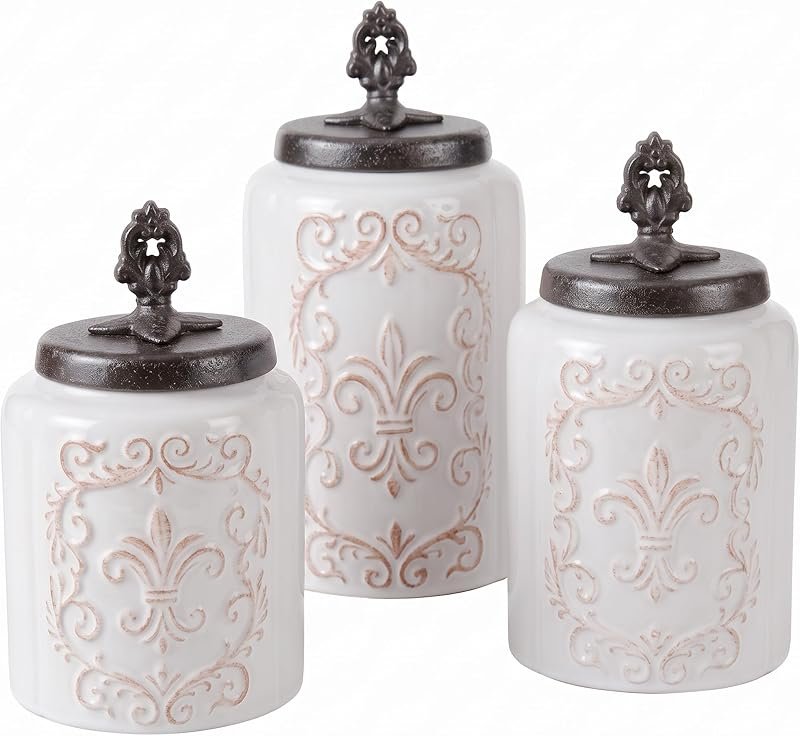 Three white ceramic kitchen canisters with fleur-de-lis pattern and dark metal lids