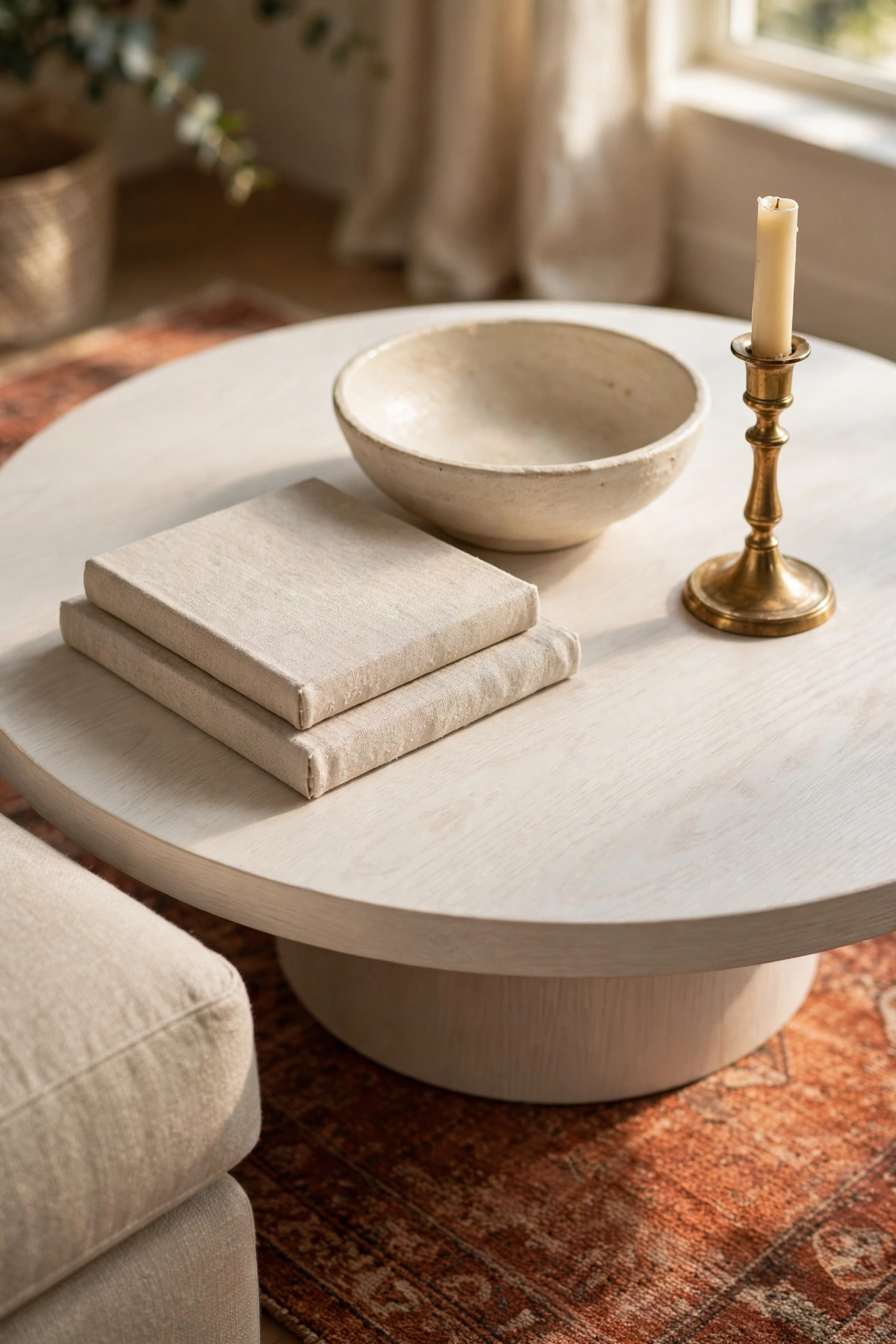 Round white oak coffee table styled with a stoneware bowl, linen books, and a brass candlestick in warm morning light
