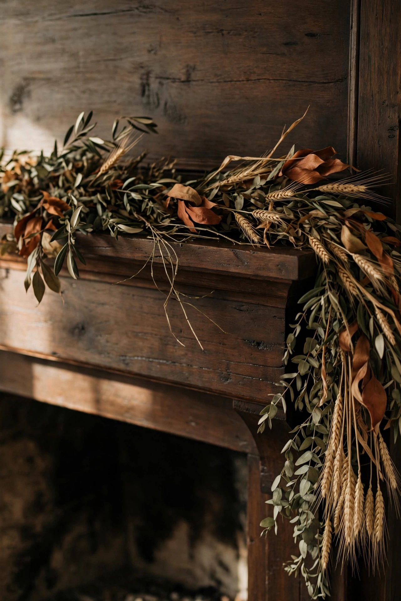Dark wood fireplace mantel with only a dried botanical garland of olive eucalyptus, rust leaves and wheat draped across it, spilling softly over one edge.